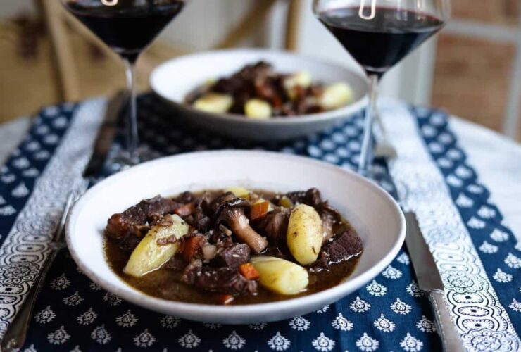 Beef Bourguignon served in rustic ceramic bowls with crusty bread, wine-dark sauce glistening, garnished with fresh herbs