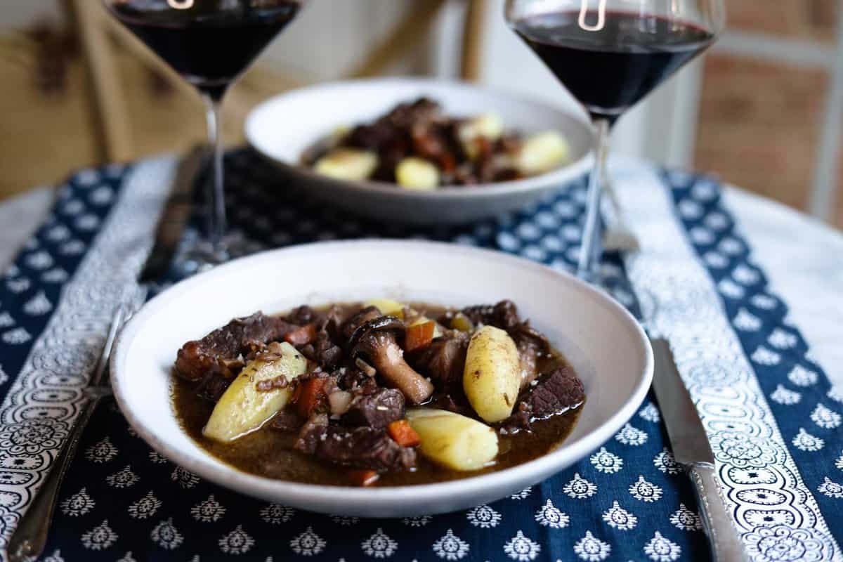 Beef Bourguignon served in rustic ceramic bowls with crusty bread, wine-dark sauce glistening, garnished with fresh herbs