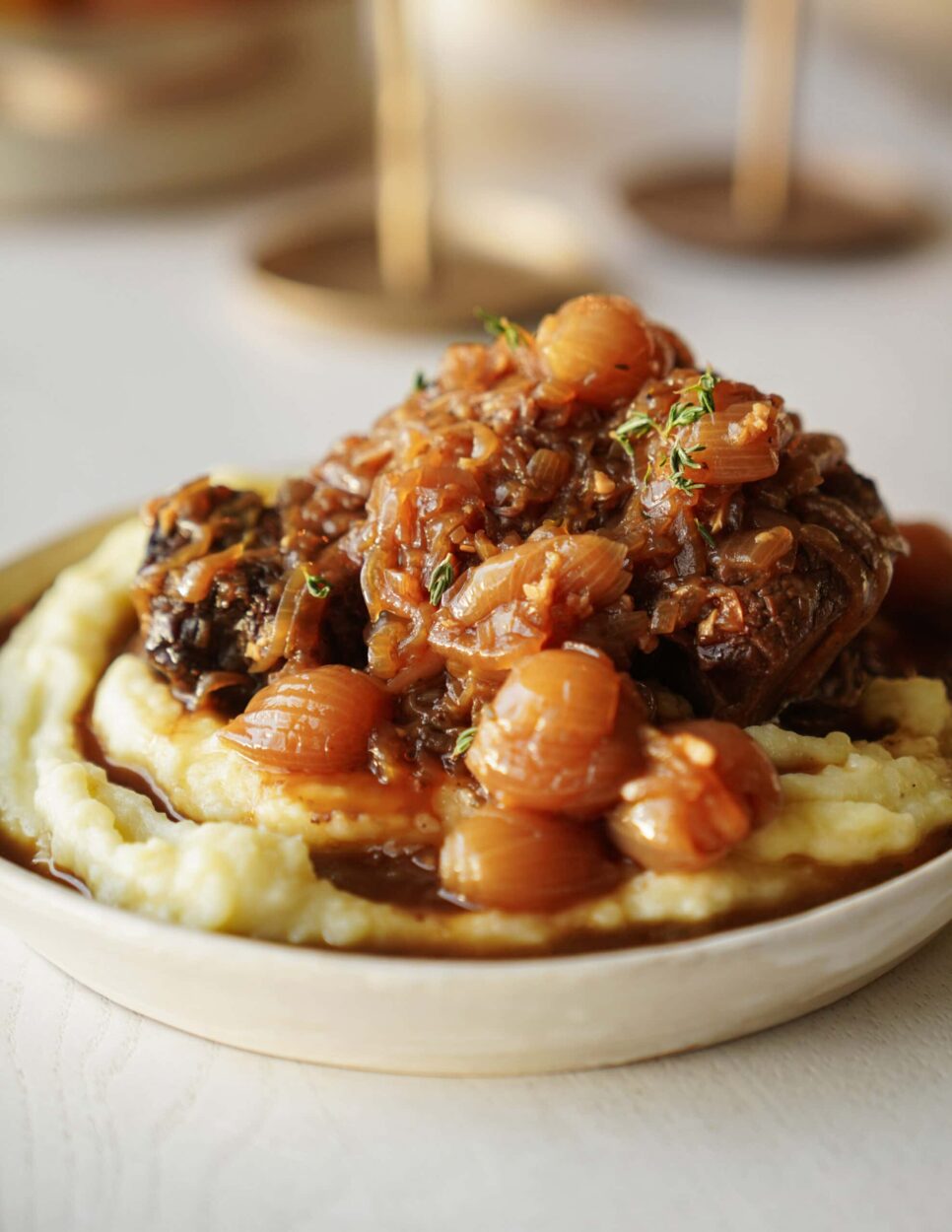 Close-up of fork-tender beef in glossy wine sauce with pearl onions and herbs, steam rising from the dish