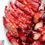 Glossy char siu pork slices arranged on white platter with chopsticks, showing the beautiful mahogany-red caramelized exterior and juicy pink interior