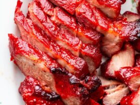 Glossy char siu pork slices arranged on white platter with chopsticks, showing the beautiful mahogany-red caramelized exterior and juicy pink interior