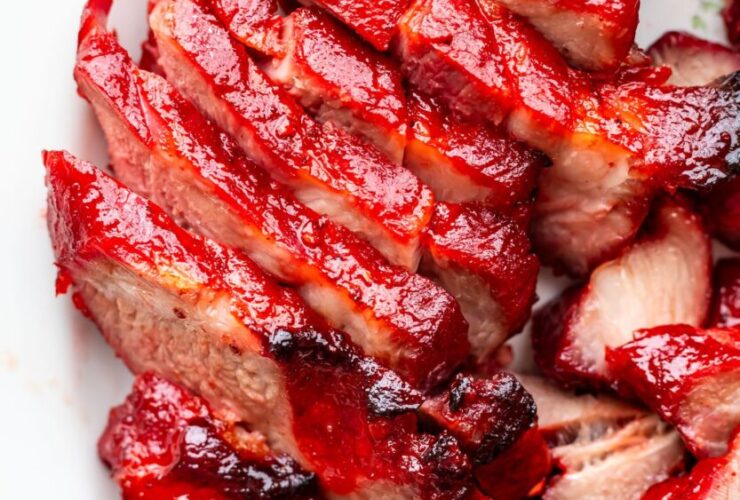Glossy char siu pork slices arranged on white platter with chopsticks, showing the beautiful mahogany-red caramelized exterior and juicy pink interior