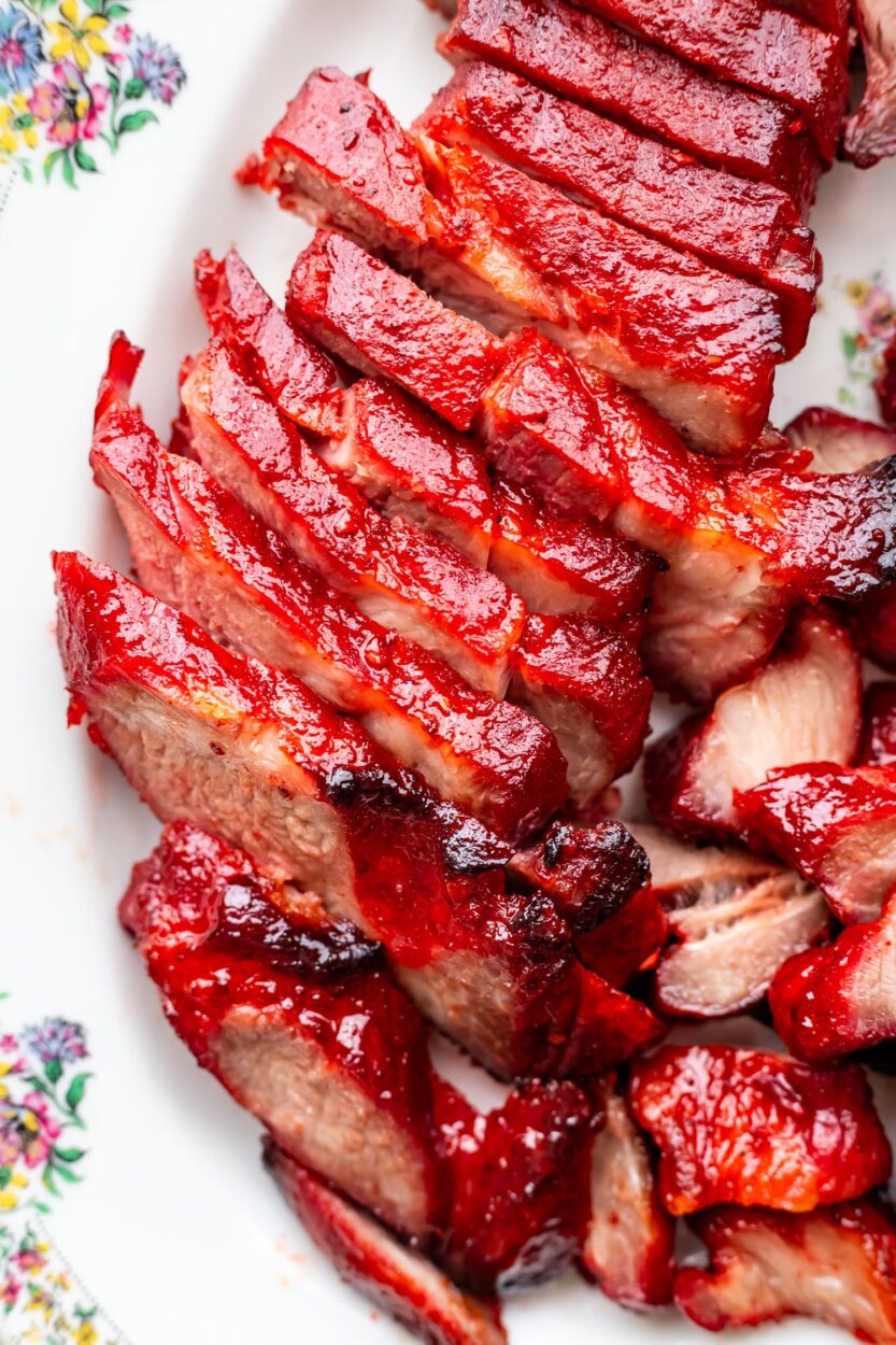Glossy char siu pork slices arranged on white platter with chopsticks, showing the beautiful mahogany-red caramelized exterior and juicy pink interior