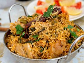 Overhead shot of golden chicken biryani in a heavy-bottomed pot with visible saffron threads, garnished with fresh cilantro and crispy onions, with a serving spoon ready to dig in