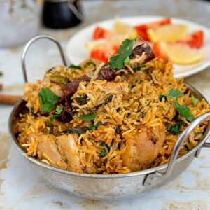 Overhead shot of golden chicken biryani in a heavy-bottomed pot with visible saffron threads, garnished with fresh cilantro and crispy onions, with a serving spoon ready to dig in