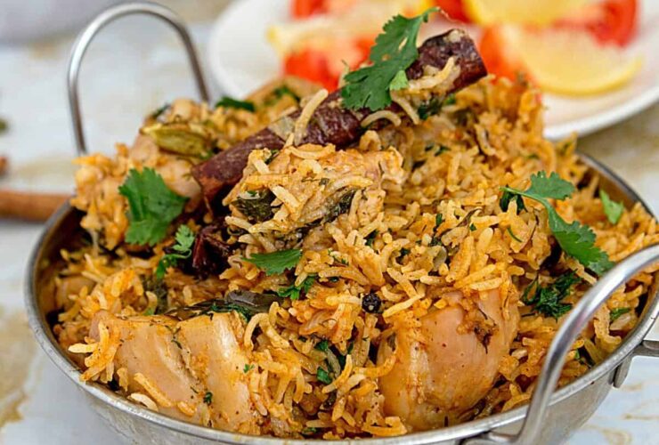 Overhead shot of golden chicken biryani in a heavy-bottomed pot with visible saffron threads, garnished with fresh cilantro and crispy onions, with a serving spoon ready to dig in