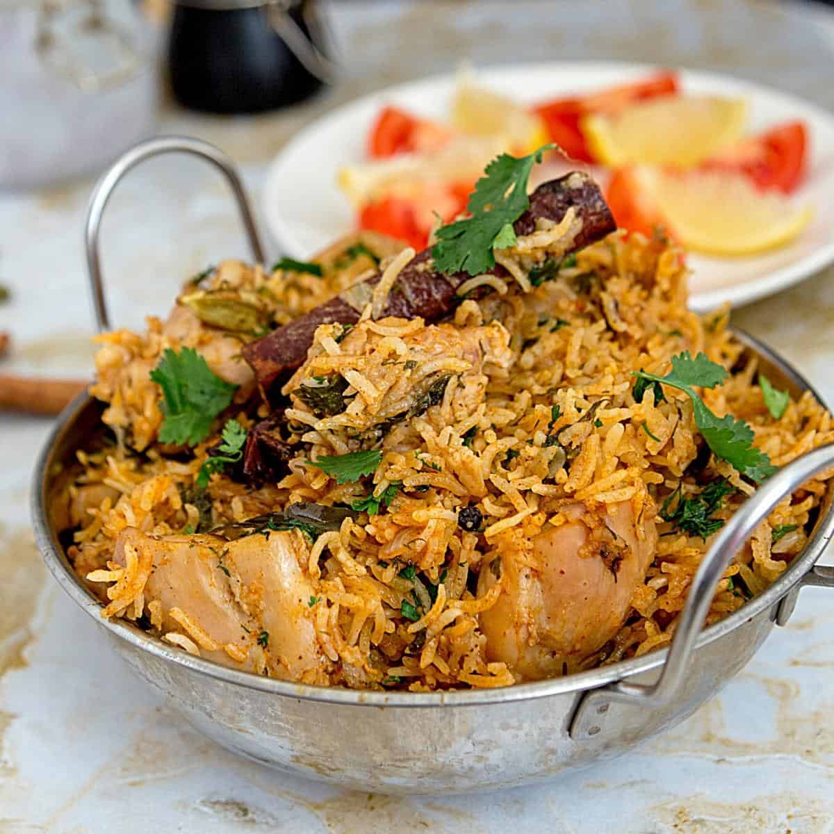 Overhead shot of golden chicken biryani in a heavy-bottomed pot with visible saffron threads, garnished with fresh cilantro and crispy onions, with a serving spoon ready to dig in