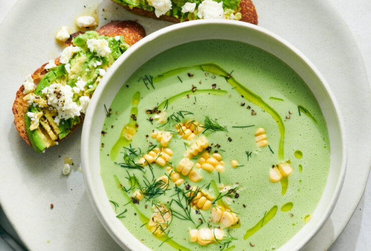 Elegant cold cucumber avocado soup served in a white ceramic bowl with a swirl of cream, fresh herbs, and a drizzle of olive oil, photographed from above on a marble surface