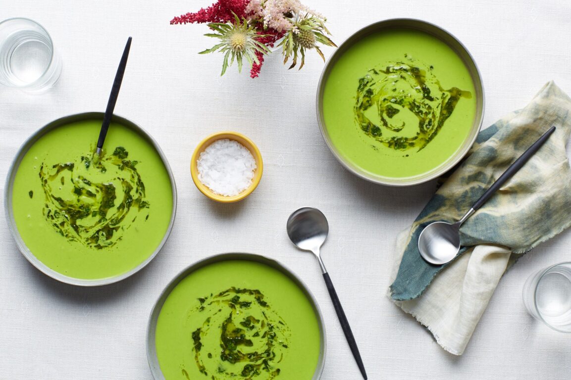 Close-up shot of cold cucumber avocado soup in an elegant bowl with a spoon, showing the creamy texture and garnish of herbs and olive oil drizzle