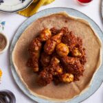 Ethiopian Doro Wat served in traditional clay bowl with injera bread, showing rich red sauce coating tender chicken with halved hard-boiled eggs