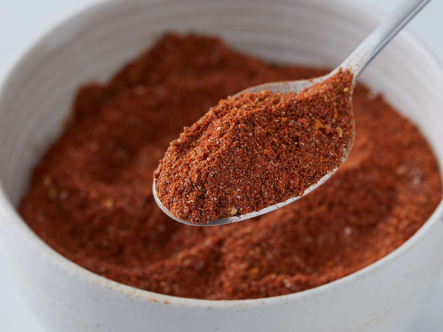 Berbere spice blend in wooden spoon with caramelized onions cooking in cast iron pan, showing the deep red color and aromatic ingredients