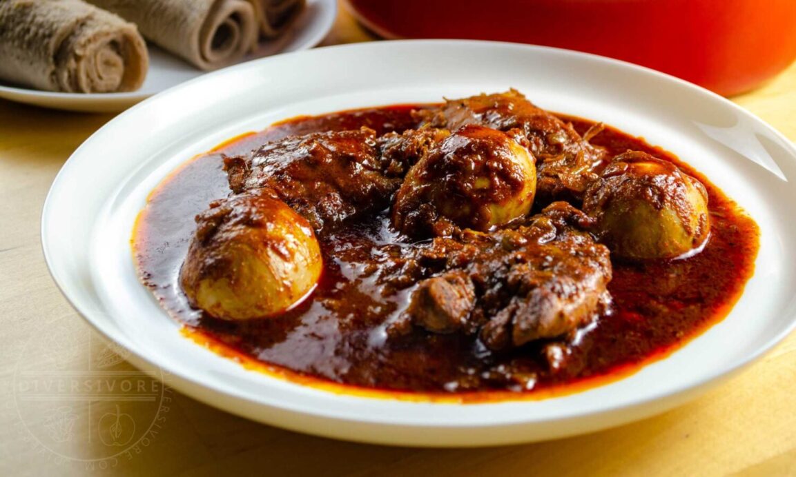 Close-up of Doro Wat showing tender chicken falling apart in rich, glossy red sauce with perfectly cooked egg half visible