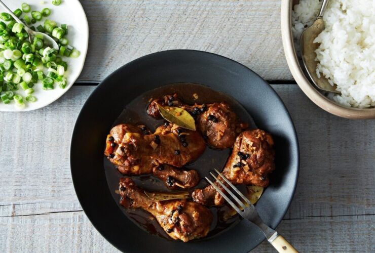 Filipino chicken adobo served in a rustic bowl with glossy dark sauce coating tender chicken pieces, garnished with fresh scallions, with steamed rice on the side