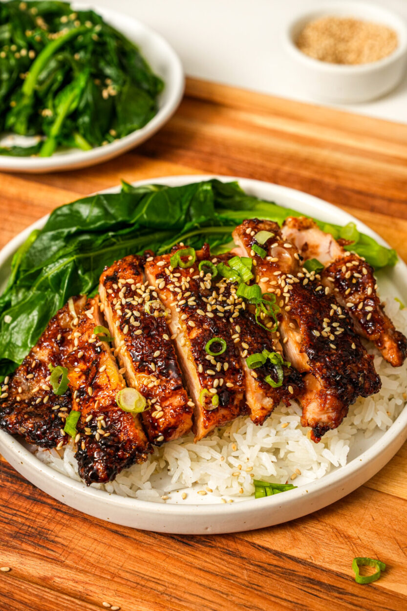Raw chicken thighs and key ingredients including soy sauce bottles, garlic cloves, bay leaves, and peppercorns arranged on a wooden cutting board