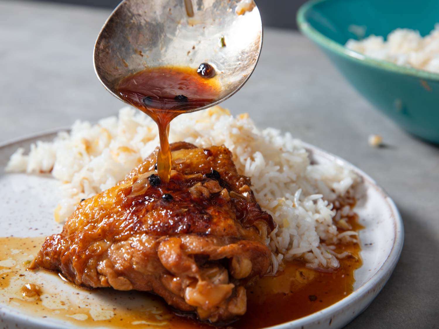 Close-up shot of a fork pulling apart tender adobo chicken with the glossy dark sauce visible, showing the fall-apart texture