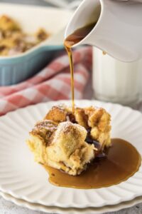 Golden French toast casserole in a white ceramic baking dish, showing perfectly puffed surface with caramelized edges and a dusting of powdered sugar