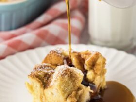 Golden French toast casserole in a white ceramic baking dish, showing perfectly puffed surface with caramelized edges and a dusting of powdered sugar