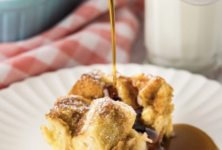 Golden French toast casserole in a white ceramic baking dish, showing perfectly puffed surface with caramelized edges and a dusting of powdered sugar
