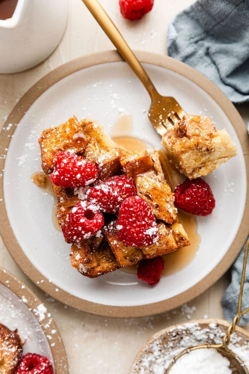 Close-up slice of French toast casserole on a white plate showing the custardy interior texture, garnished with fresh berries and a drizzle of maple syrup