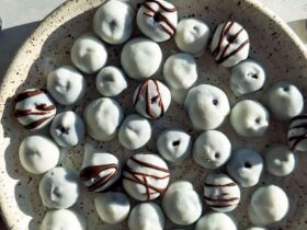 A beautiful overhead shot of frozen yogurt covered blueberries arranged on a white marble surface, glistening with a creamy yogurt shell, scattered with fresh blueberries and mint leaves for garnish