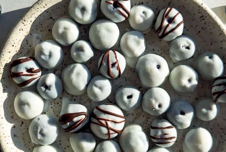 A beautiful overhead shot of frozen yogurt covered blueberries arranged on a white marble surface, glistening with a creamy yogurt shell, scattered with fresh blueberries and mint leaves for garnish