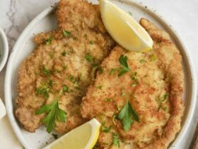 Golden brown German schnitzel on an elegant white plate, garnished with fresh lemon wedges and parsley, with a side of crispy potatoes