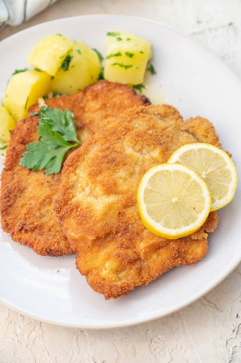 Close-up shot of sliced German schnitzel showing the golden, crispy coating and juicy interior, with a fork cutting through, served alongside traditional German sides