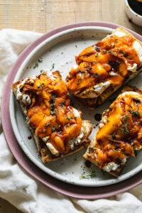 Grilled peach burrata breakfast toast beautifully plated with golden caramelized peaches, creamy burrata, fresh herbs, and drizzled honey on rustic wooden board