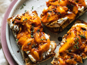 Grilled peach burrata breakfast toast beautifully plated with golden caramelized peaches, creamy burrata, fresh herbs, and drizzled honey on rustic wooden board