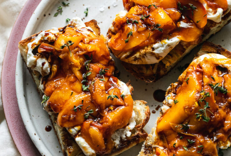 Grilled peach burrata breakfast toast beautifully plated with golden caramelized peaches, creamy burrata, fresh herbs, and drizzled honey on rustic wooden board