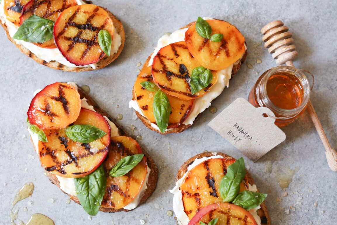 Close-up shot of the finished toast showing the creamy burrata texture, caramelized peach details, and fresh herb garnish with honey drizzle