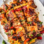 Grilled pineapple chicken skewers served on a wooden board with charred pineapple chunks, fresh herbs, and a side of dipping sauce