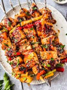 Grilled pineapple chicken skewers served on a wooden board with charred pineapple chunks, fresh herbs, and a side of dipping sauce