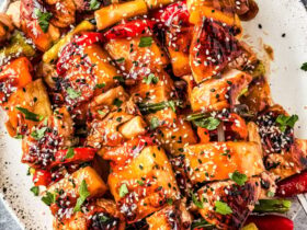 Grilled pineapple chicken skewers served on a wooden board with charred pineapple chunks, fresh herbs, and a side of dipping sauce