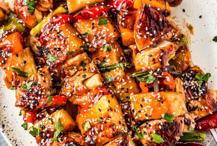 Grilled pineapple chicken skewers served on a wooden board with charred pineapple chunks, fresh herbs, and a side of dipping sauce