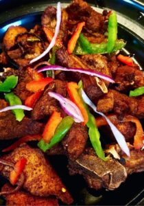 Crispy golden Haitian griot pork chunks garnished with fresh herbs on a rustic wooden plate with lime wedges and pikliz