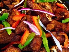 Crispy golden Haitian griot pork chunks garnished with fresh herbs on a rustic wooden plate with lime wedges and pikliz