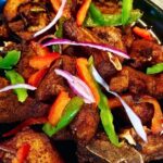 Crispy golden Haitian griot pork chunks garnished with fresh herbs on a rustic wooden plate with lime wedges and pikliz