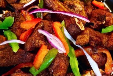 Crispy golden Haitian griot pork chunks garnished with fresh herbs on a rustic wooden plate with lime wedges and pikliz