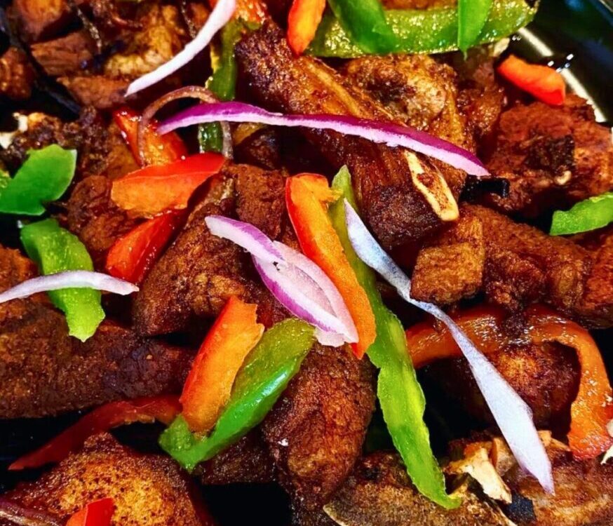 Crispy golden Haitian griot pork chunks garnished with fresh herbs on a rustic wooden plate with lime wedges and pikliz