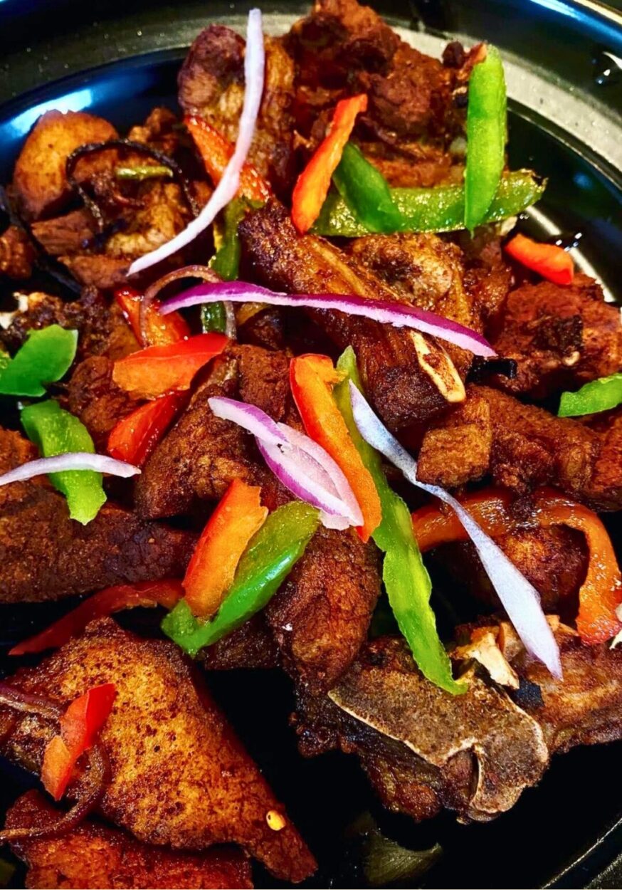 Crispy golden Haitian griot pork chunks garnished with fresh herbs on a rustic wooden plate with lime wedges and pikliz