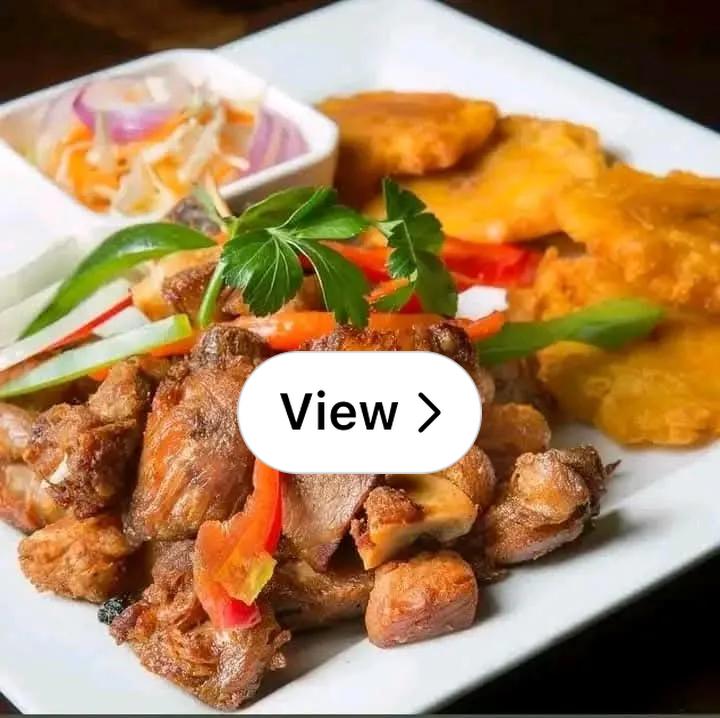 Close-up of crispy griot served over white rice with colorful pikliz and fried plantains on the side