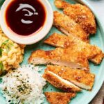 Golden crispy Japanese chicken katsu cutlets arranged on a white plate with shredded cabbage, katsu sauce, and lemon wedges, photographed from above with dramatic lighting