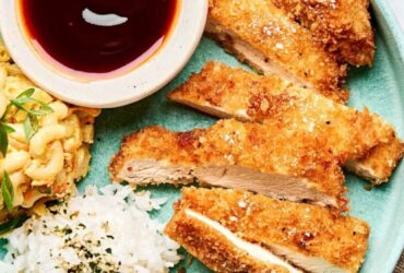 Golden crispy Japanese chicken katsu cutlets arranged on a white plate with shredded cabbage, katsu sauce, and lemon wedges, photographed from above with dramatic lighting