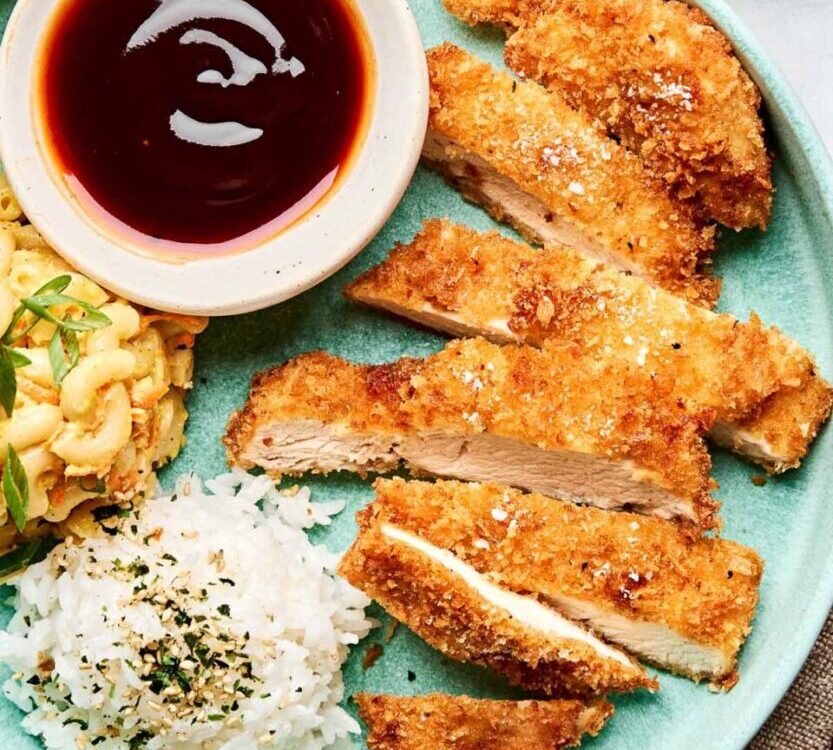 Golden crispy Japanese chicken katsu cutlets arranged on a white plate with shredded cabbage, katsu sauce, and lemon wedges, photographed from above with dramatic lighting
