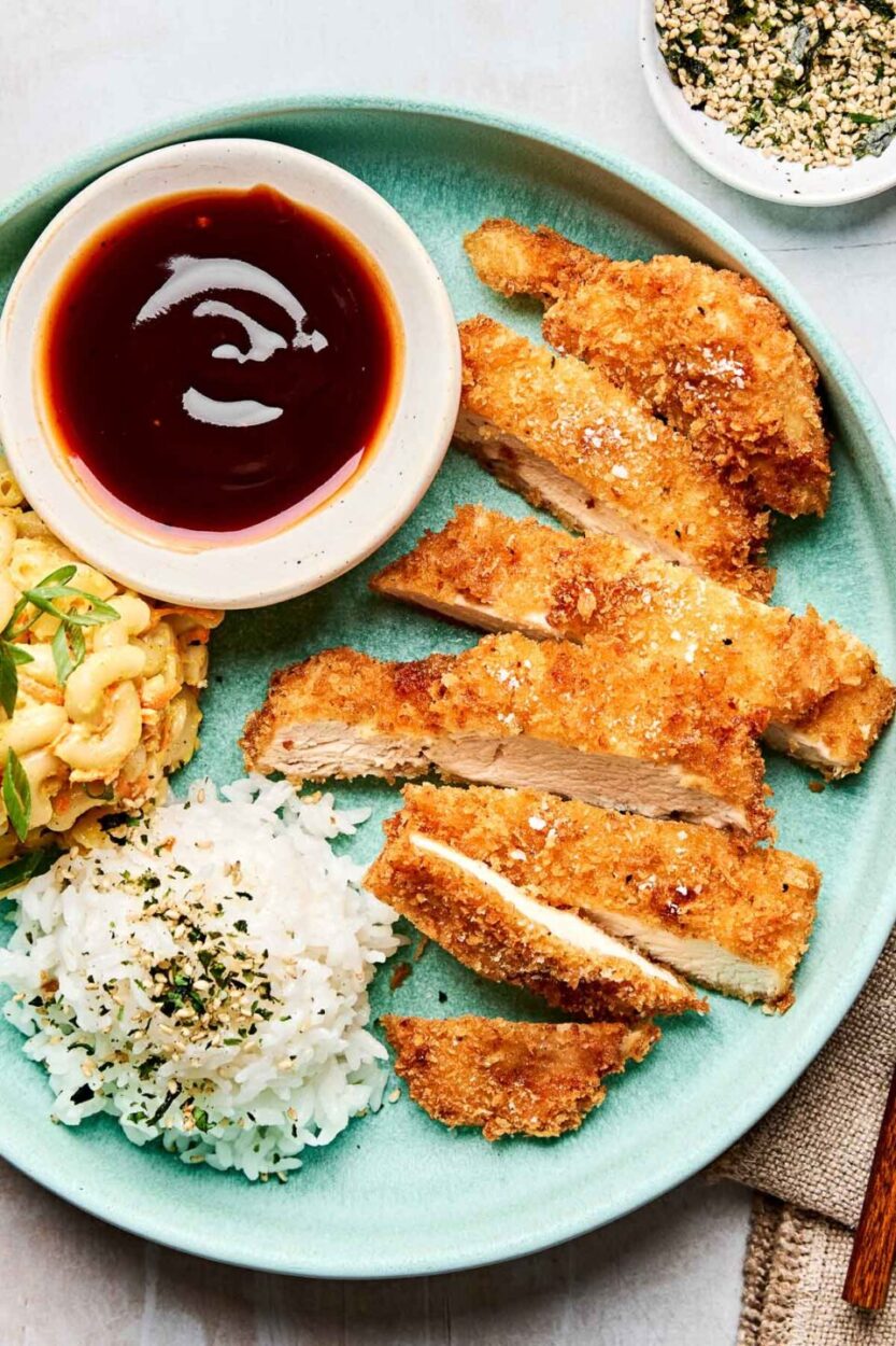 Golden crispy Japanese chicken katsu cutlets arranged on a white plate with shredded cabbage, katsu sauce, and lemon wedges, photographed from above with dramatic lighting