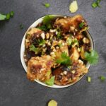 Close-up shot of Kung Pao Chicken on chopsticks, showing the glossy sauce coating and visible Sichuan peppercorns and dried chilies, with steam rising