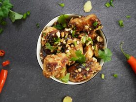 Close-up shot of Kung Pao Chicken on chopsticks, showing the glossy sauce coating and visible Sichuan peppercorns and dried chilies, with steam rising