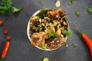 Close-up shot of Kung Pao Chicken on chopsticks, showing the glossy sauce coating and visible Sichuan peppercorns and dried chilies, with steam rising