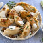 Golden Polish pierogi arranged on a rustic wooden plate, topped with caramelized onions and fresh herbs, with melted butter glistening on top